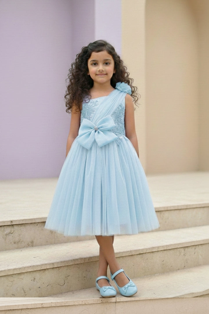 A young girl in a light blue dress from Nibblekins with a large bow is standing on the steps.