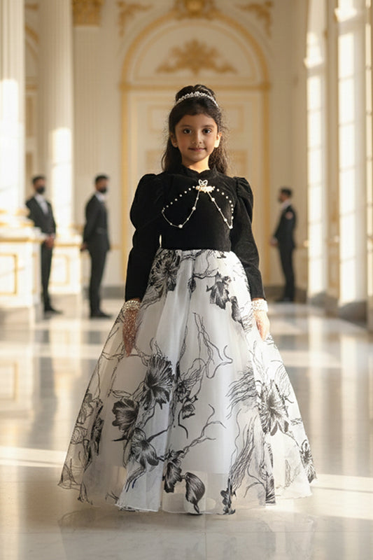 A Young girl in a black and white floral gown from Nibblekins is standing in an elegant hall with people in formal attire.