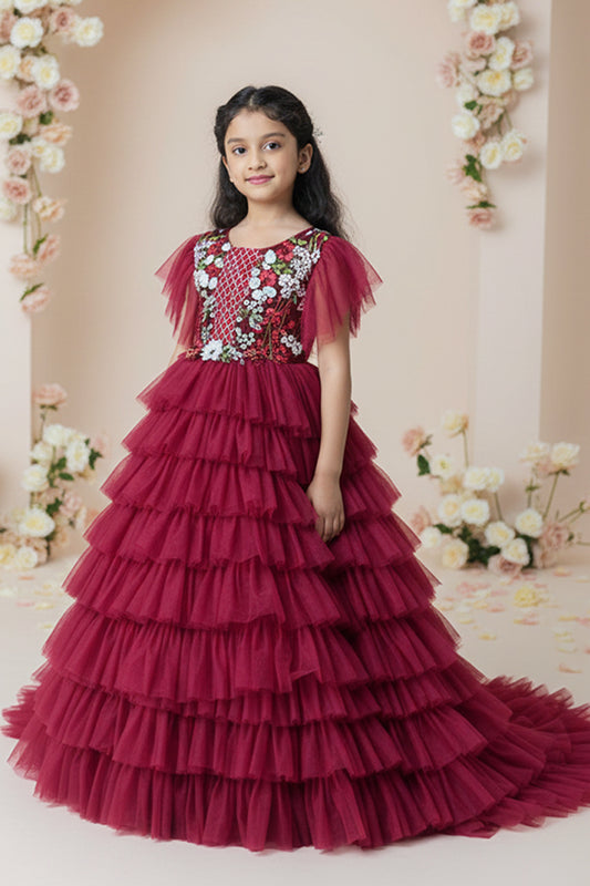 A Young girl in a red layered dress from Nibblekins with floral embellishments against a floral decorated background
