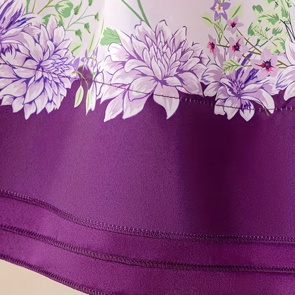 A close-up of a purple fabric product, likely a tablecloth or napkin, featuring a solid purple border and a floral print of large white and purple flowers with green leaves on a pale pink background.
