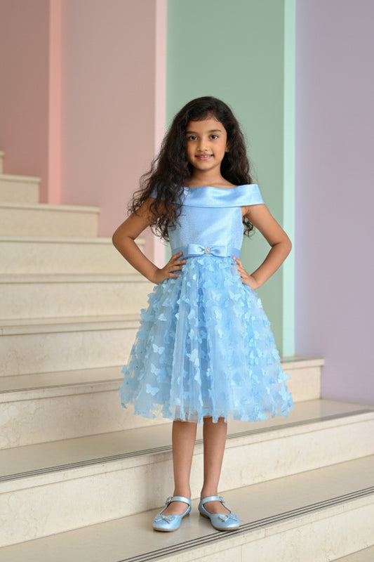 A young girl in a light blue dress from nibblekins standing on a staircase with pastel-colored walls.