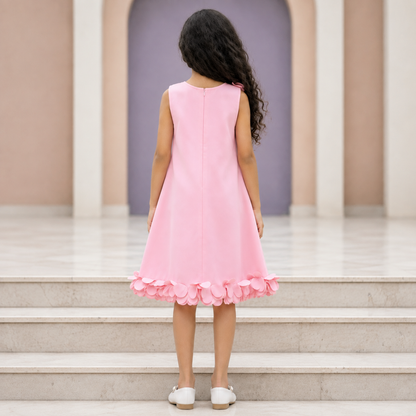 A young girl with long curly black hair is shown from behind, wearing a sleeveless light pink dress with a ruffled hem, standing on stone steps in front of a purple archway.