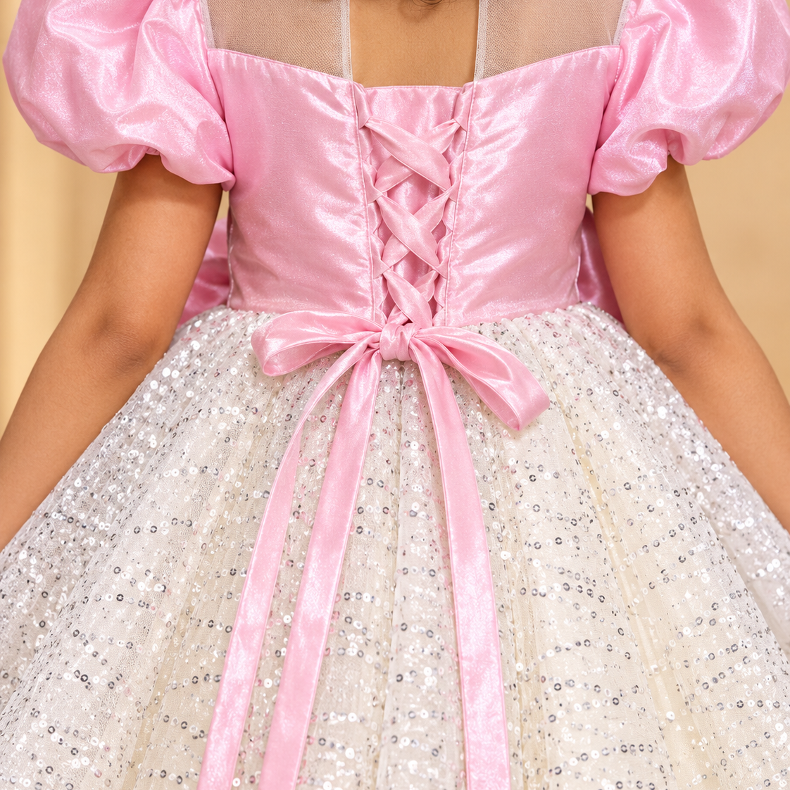 A close-up back view of a child wearing a pink and white sequined ball gown costume. The dress features a shiny pink satin bodice with puff sleeves, a lace-up back, and a voluminous white tulle skirt covered in silver sequins.