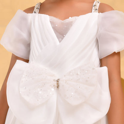 A close-up of a white formal dress with sheer puff sleeves, a V-neckline, and a large bow detail on the front covered in silver sequins and embellishments.