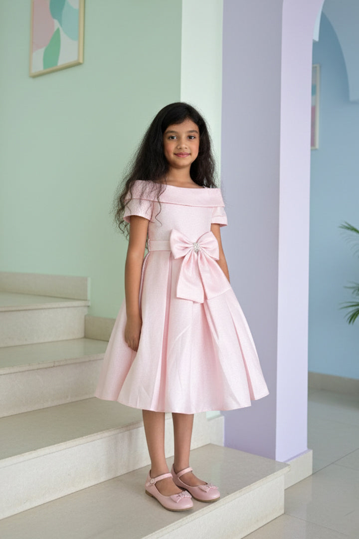 A young girl in a pink dress from Nibblekins is standing on a staircase with a light blue wall and white steps in the background.