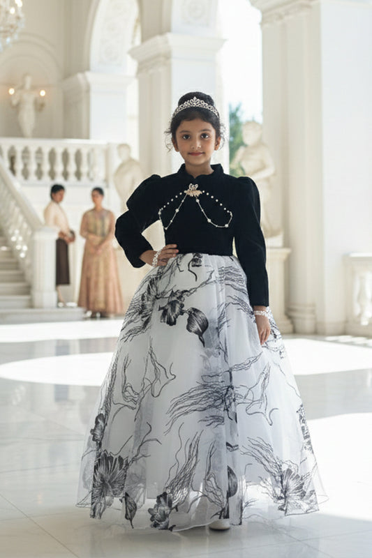 A young girl in a black and white floral gown from Nibblekins is standing in an elegant interior setting.