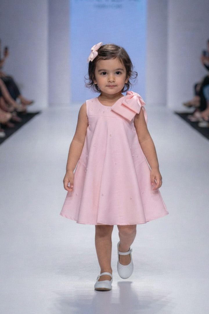 A young child in a pink dress from Nibblekins walking on a runway