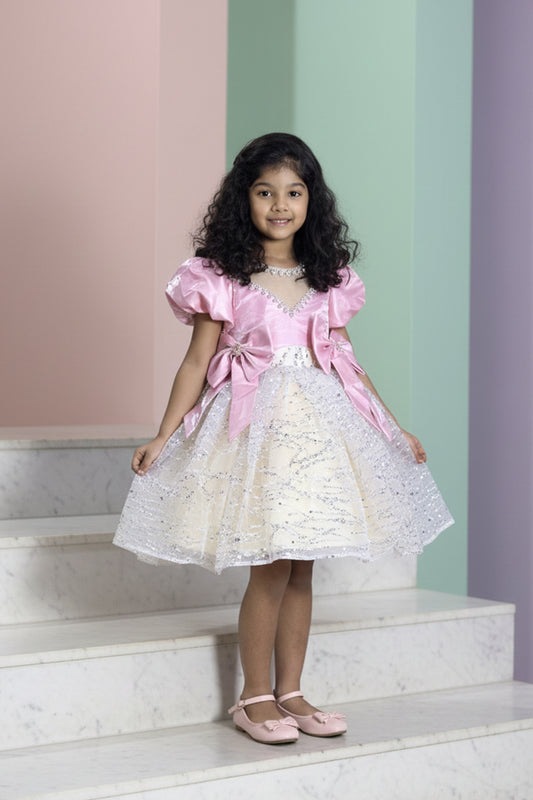A Young girl in a pink and ivory dress with glitter from nibblekins standing on steps with a colorful wall background