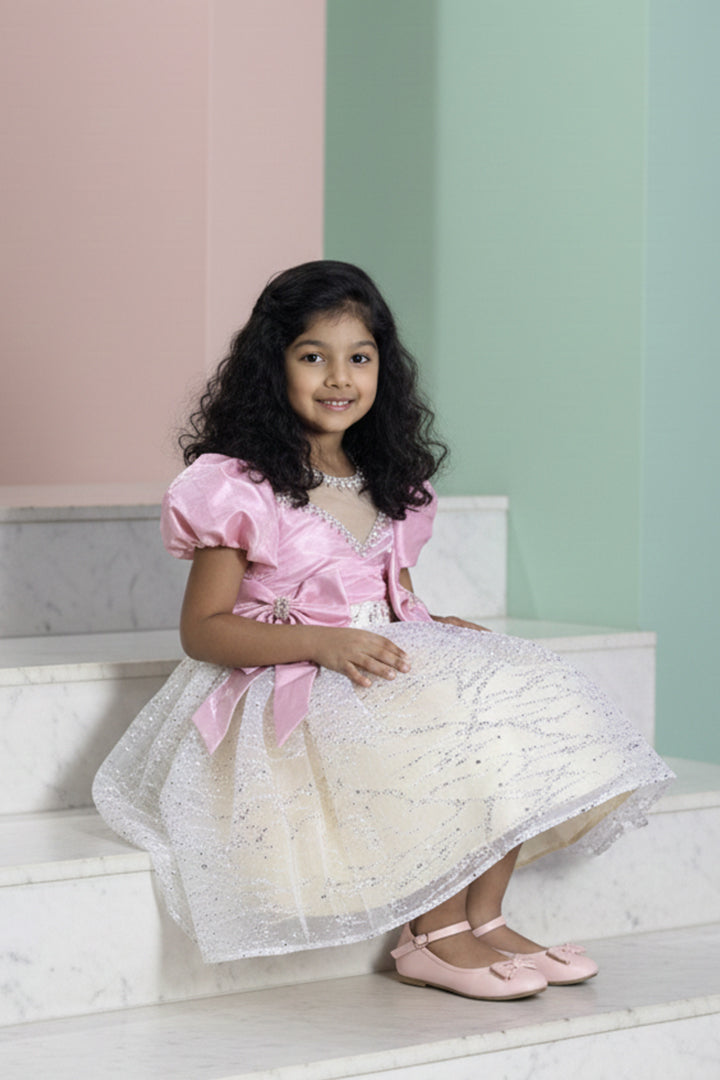 A Young girl in a pink and ivory dress with glitter from nibblekins, sitting on steps with a pastel-colored wall background