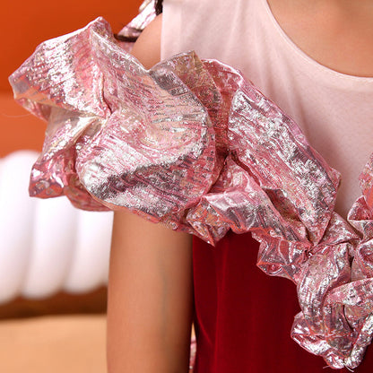 Close-up of a person wearing a white top with pink ruffled sleeves against an orange background