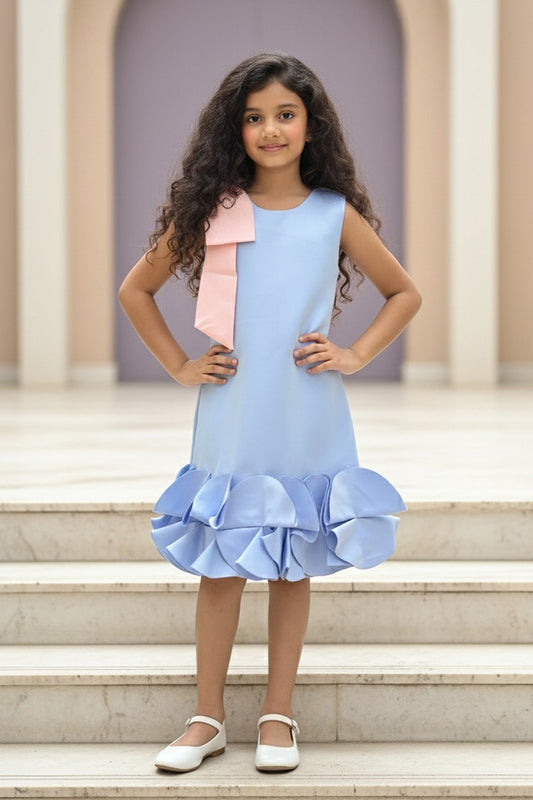 A Young girl wearing a light blue dress from Nibblekins with a ruffled hem on the stone steps.