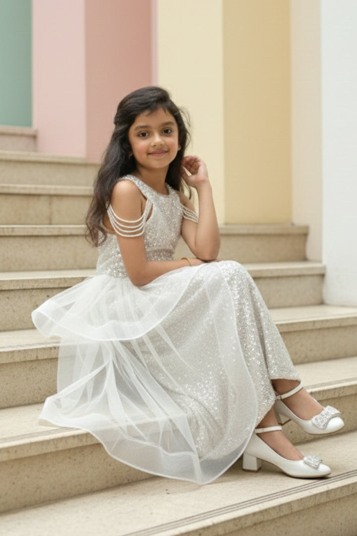 A Young girl in a white sequin dress from Nibblekins sitting on the steps with a colorful wall in the background