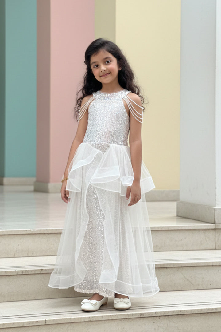 A Young girl in a white sequin dress from Nibblekins standing on steps with a colorful wall in the background