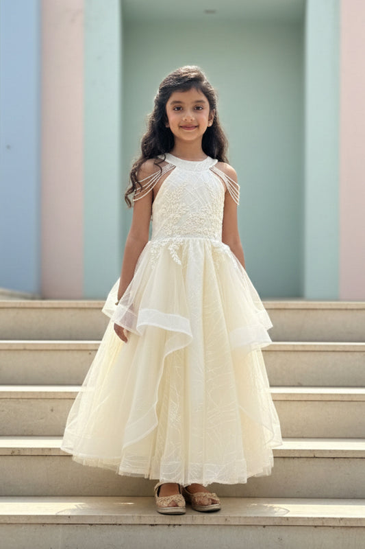 Young girl in an Off white dress from Nibblekins standing on steps with a pastel-colored wall in the background