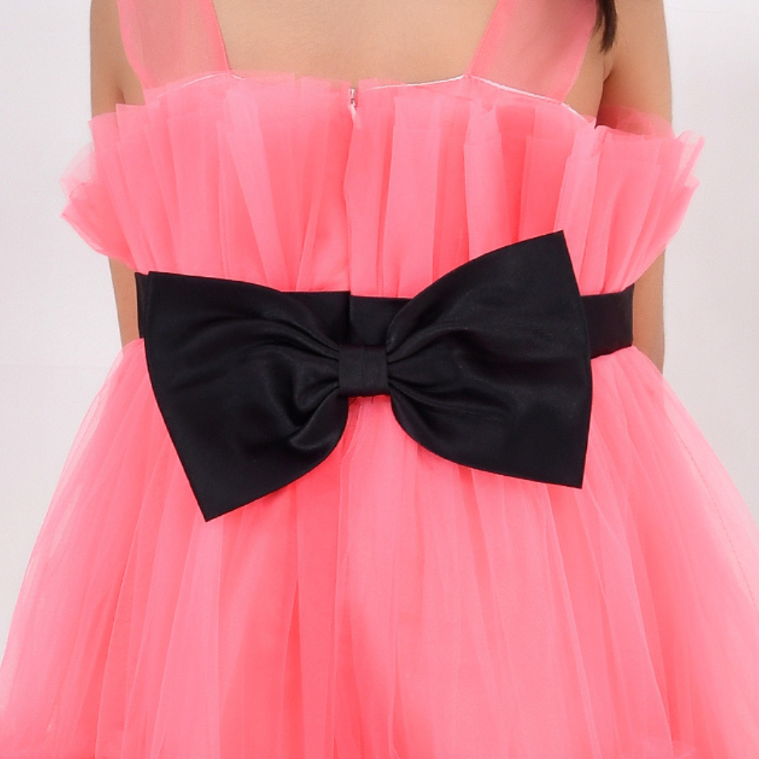A close-up of a bright pink tulle dress with a large black satin bow at the waist, worn by a model against a plain light background.