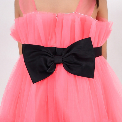 A close-up of a bright pink tulle dress with a large black satin bow at the waist, worn by a model against a plain light background.