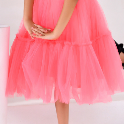 A close-up of a child wearing a bright pink tiered tulle dress, showing the layered mesh skirt and hands clasped in front.