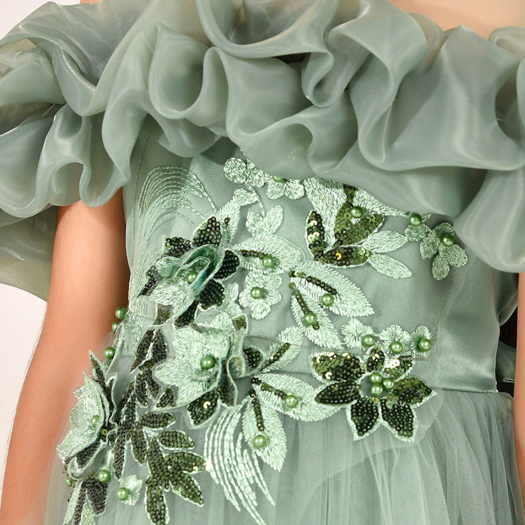 Close-up of a formal dress with a ruffled off-the-shoulder neckline and a tulle skirt, decorated with green and white floral beadwork and sequins.