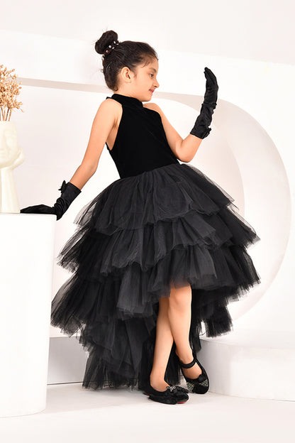Young girl in a black high low dress with a layered skirt and gloves posing against a white background
