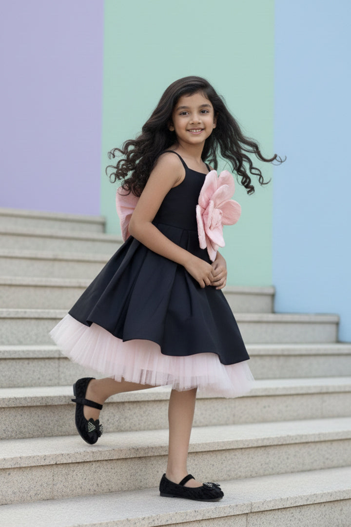 Young girl in a black dress with pink floral details standing on steps against a colorful wall nibblekins