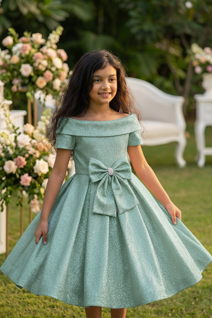 Young girl in a light blue dress with a large bow standing outdoors with floral decorations.
