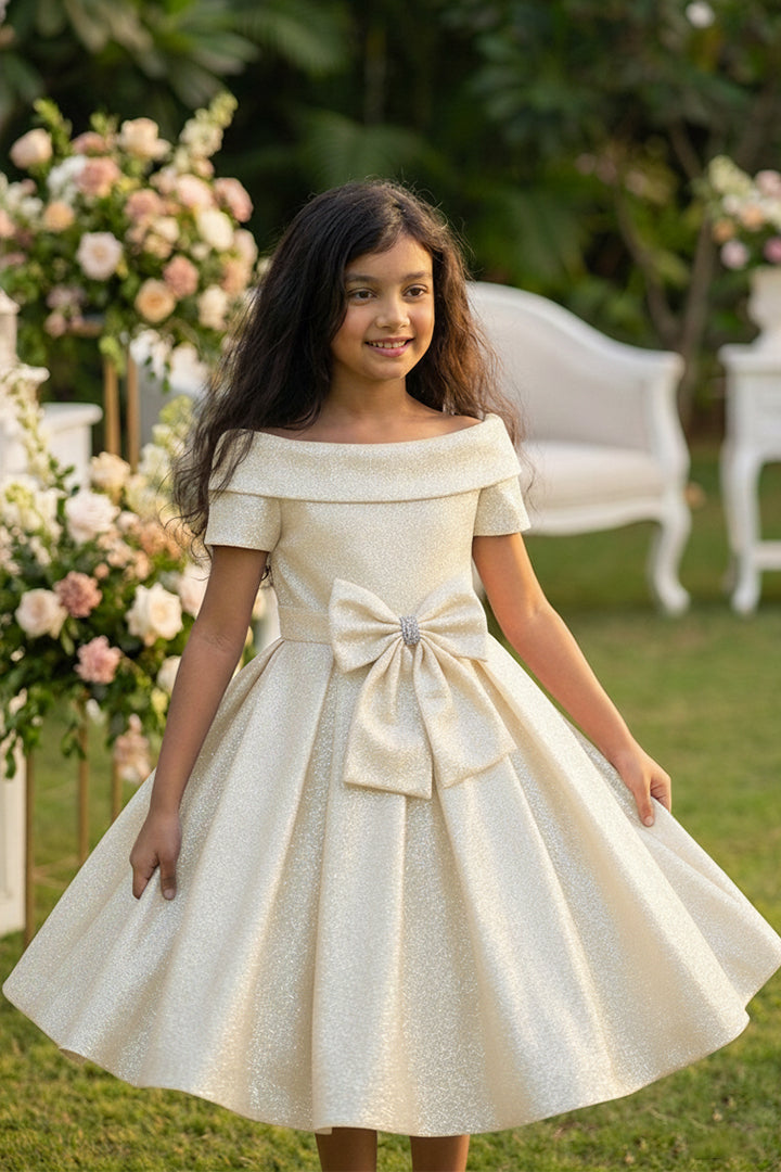 Young girl in a white dress with a bow standing outdoors with floral decorations.