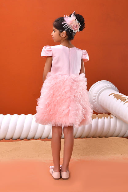 Young girl in a pink dress with a feathered headband standing against an orange background