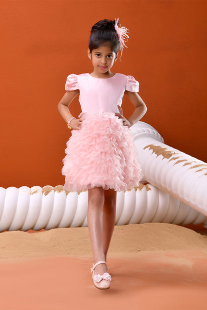 Young girl in a pink dress standing on a sandy surface with an orange background