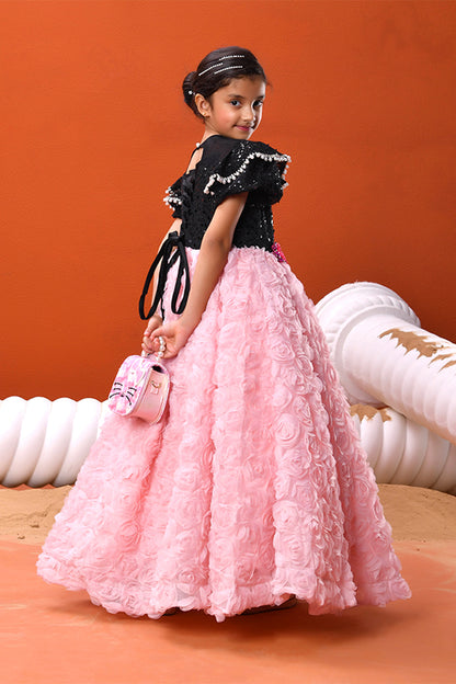 Young girl in wearing a black and pink ball gown with rose details standing against an orange background