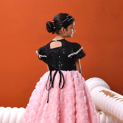 Young girl in a wearing a black and pink gown standing against an orange background