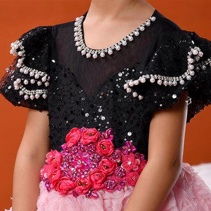 Child wearing a black and pink dress with floral details against an orange background