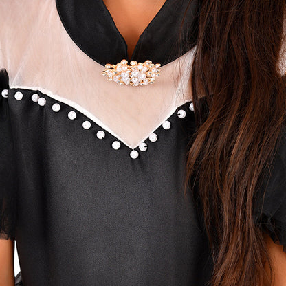 close up of Black and white gown with pearl detailing, white trim and a brooch worn by a young girl