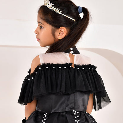 Young girl wearing a black and white dress with ruffles and a tiara on a plain background