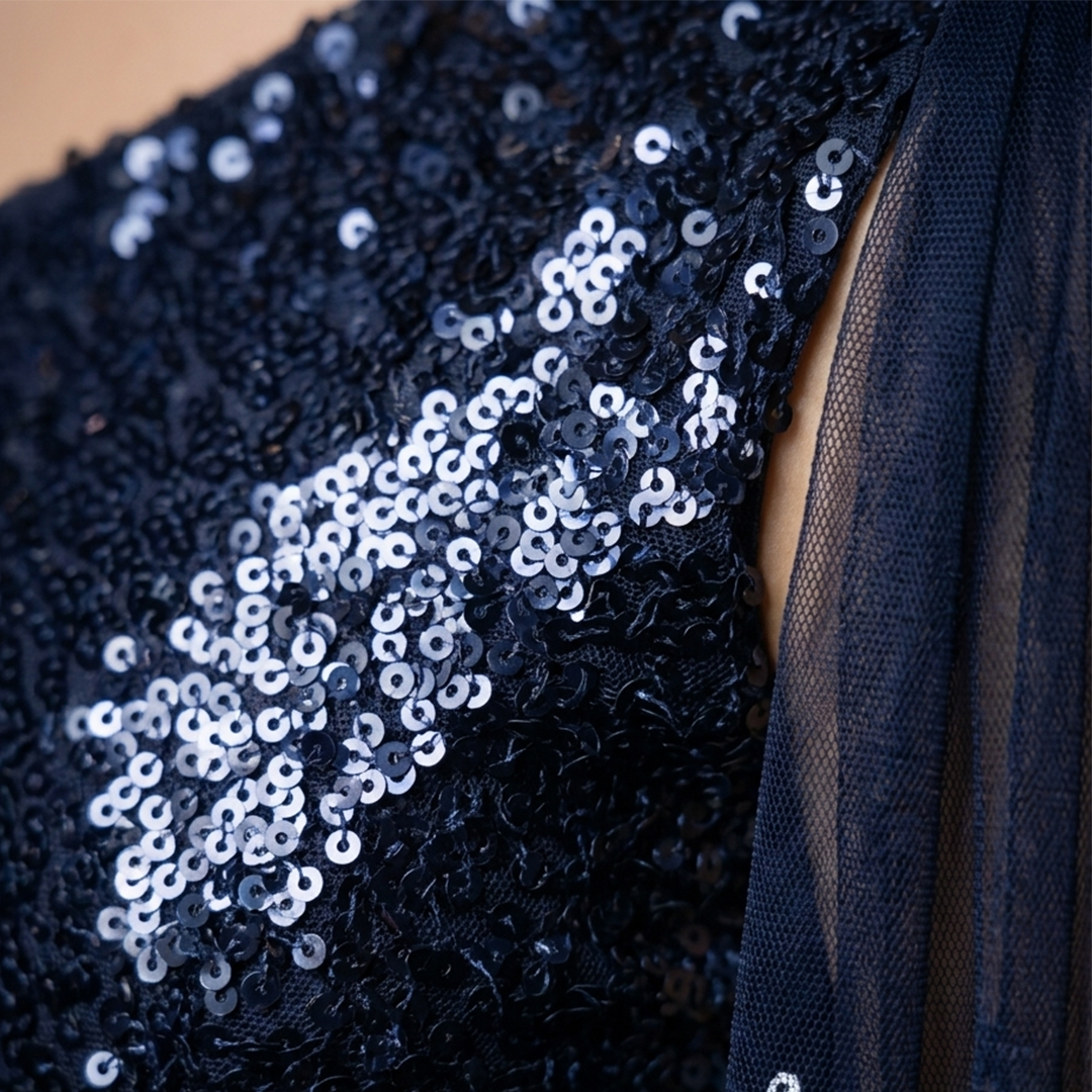 Close-up of a dark navy sequined garment with a sheer navy tulle panel, showing the texture of the sequins and fabric.