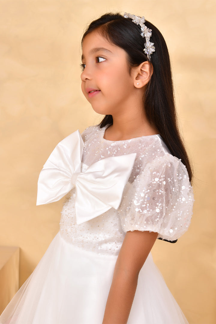 Young girl wearing a white sequin dress with a large bow on a beige background