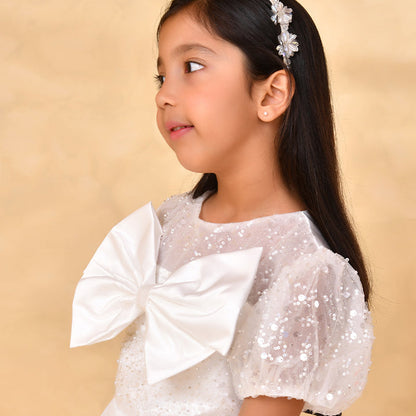 Young girl wearing a white sequin dress with a large bow on a beige background