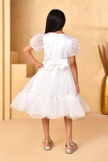 Young girl wearing a white dress with a bow, standing against a beige background