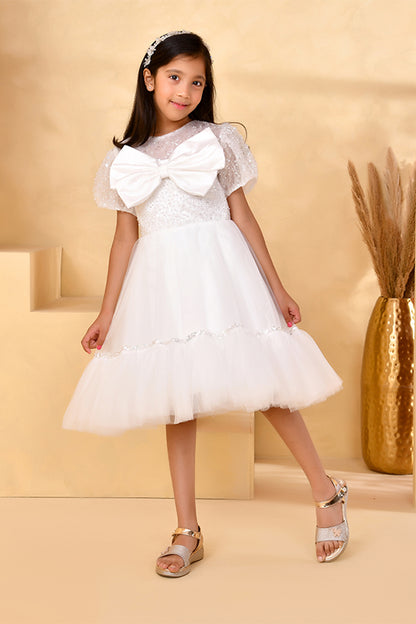 Young girl wearing a white lace dress with a large bow on a beige background