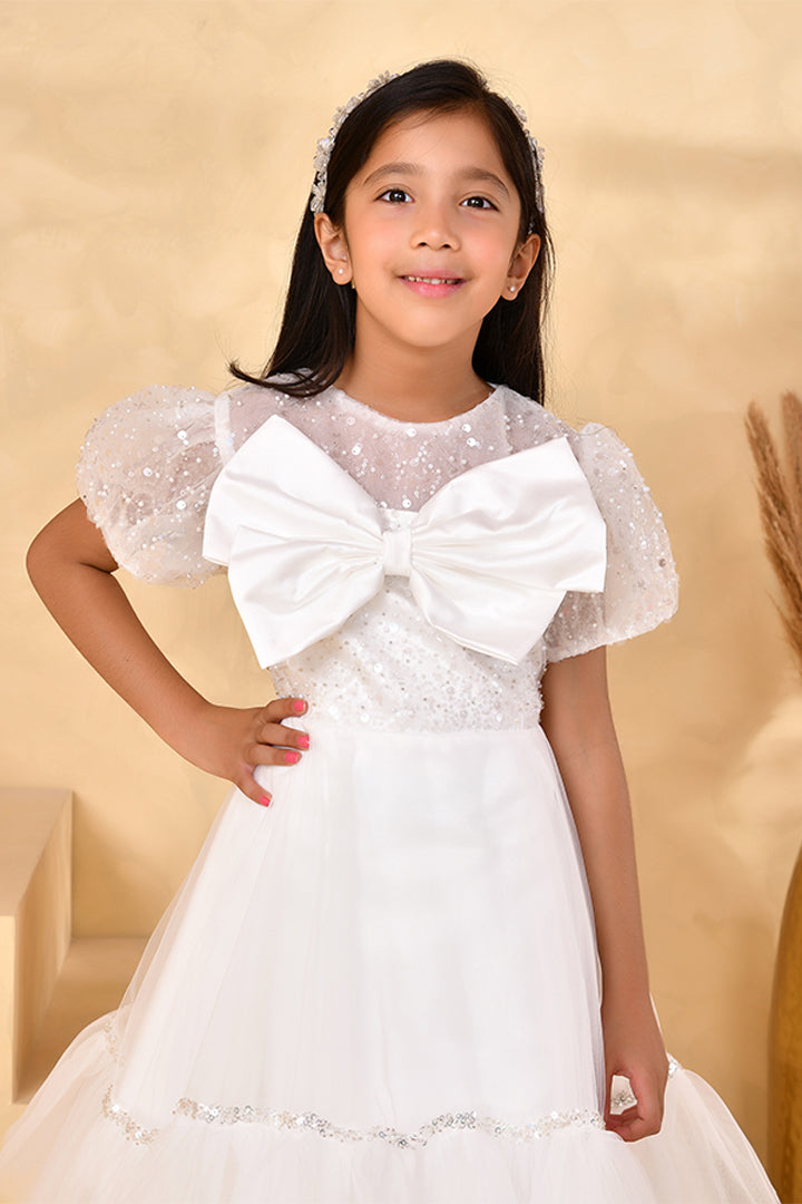 Young girl wearing a white dress with a large bow on a beige background