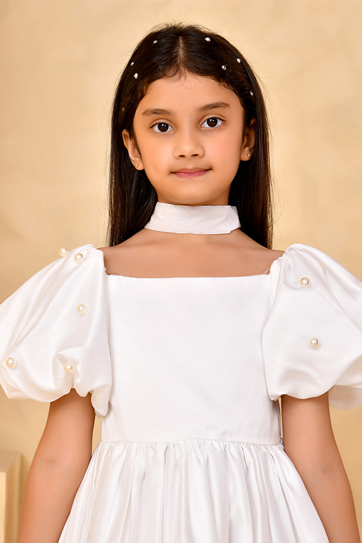 Young girl wearing a white dress with pearl details against a beige background