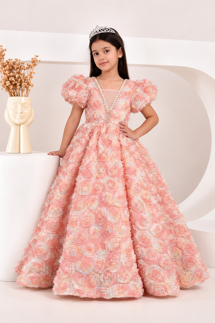 A young girl wearing a formal pink ball gown with 3D rose texture, puff sleeves, and a pearl-trimmed V-neckline, standing in a studio setting.