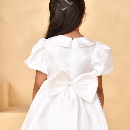 White dress with a large bow on the back worn by a person against a beige background
