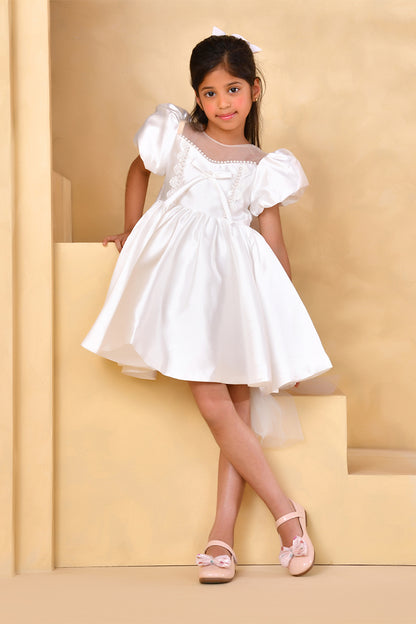 Young girl in a white dress standing against a beige background