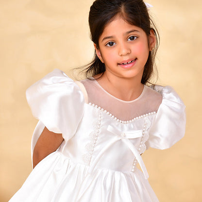 Young girl wearing a white dress with puffed sleeves against a beige background