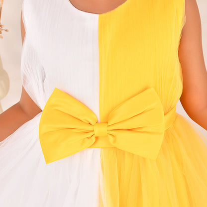 Woman wearing a white top and yellow dress with a large bow detail.