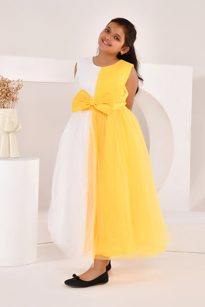 Young girl wearing a yellow and white dress with a bow, sitting on a white couch.